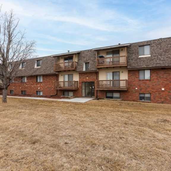apartment building with brown brick exterior and a large grassy area in front.