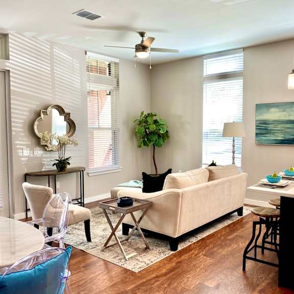 a living room with two windows, hardwood-style flooring, a ceiling fan, double doors leading to a private patio, and access to a dining area and kitchen.