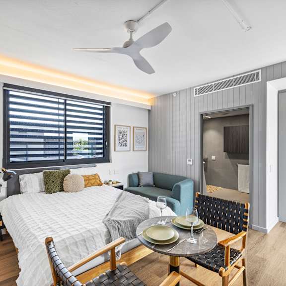 a bedroom with a bed, a chair, a table, and a ceiling fan.