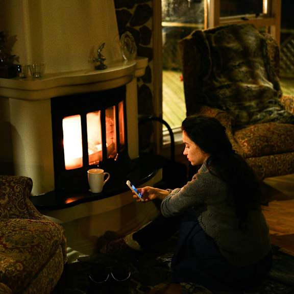 a woman sitting on the floor in front of a lit fireplace.