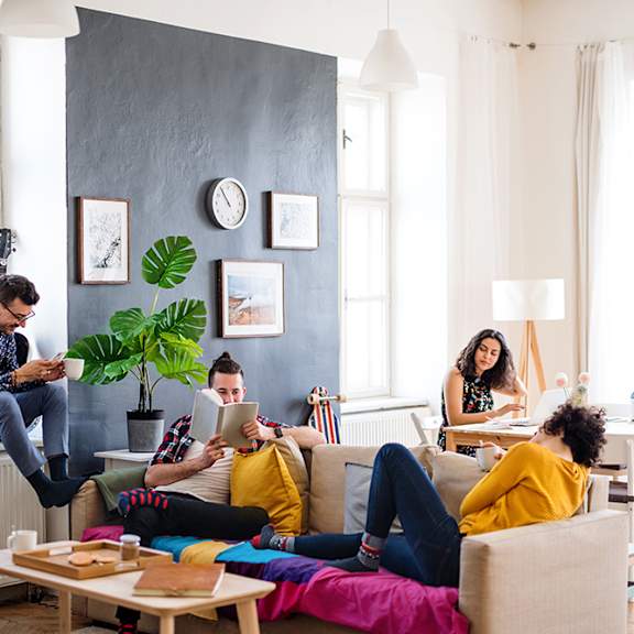 a group of people sitting in a living room reading and using laptops