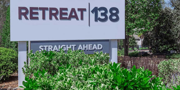 A sign for Retreat 138 Straight Ahead is displayed in front of some greenery.