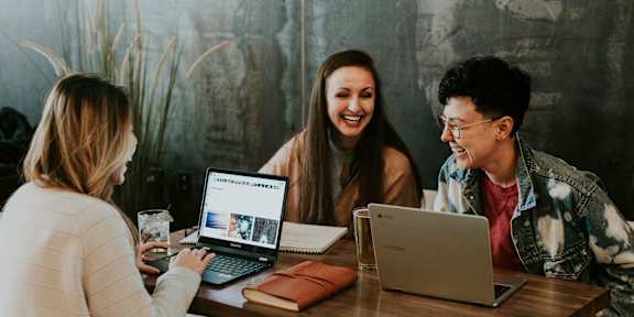 Three people are sitting at a table with laptops open in front of them.