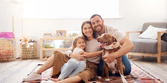A family of three with a dog sitting on a rug in a living room.