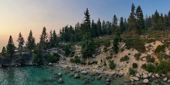 A sunset view of a rocky coastline with trees and the ocean.
