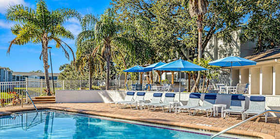 A pool surrounded by palm trees and blue umbrellas.