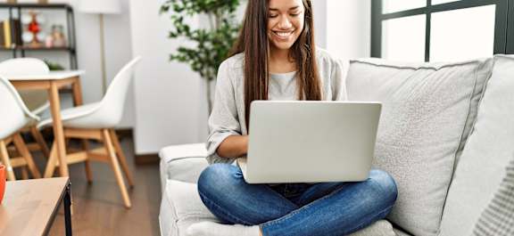 A woman is sitting on a couch using a laptop.