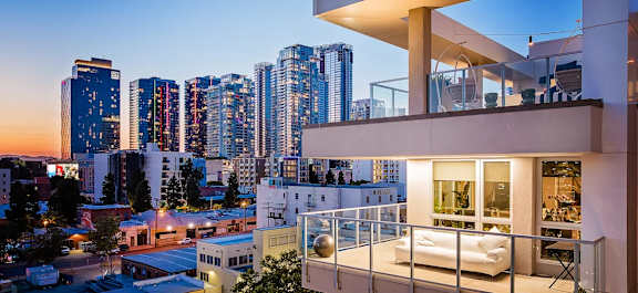 A modern apartment building with a balcony overlooking a city skyline at dusk.