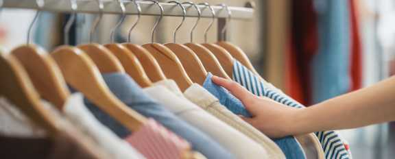 A person is holding a striped shirt in front of a rack of clothes.