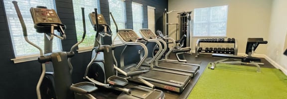 a gym with cardio equipment and a green carpet