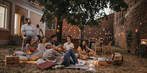 A group of people are sitting and standing around a fire in a backyard.