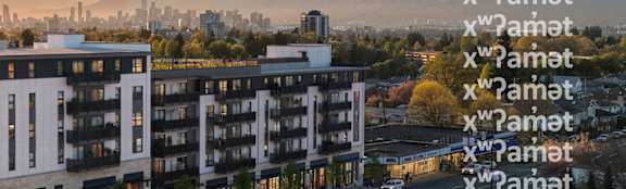 A modern apartment building with balconies and a view of a city skyline at sunset.