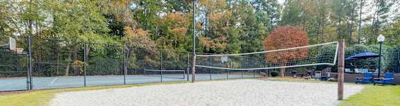 A sandy volleyball court surrounded by a fence and trees.