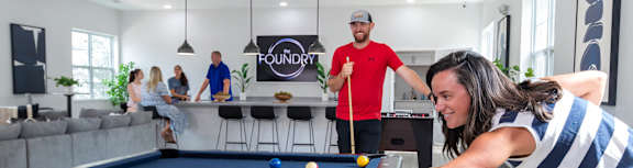 A woman is playing pool in a room with a pool table and a sign that says "FOUNDRY".