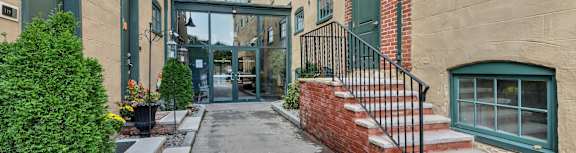 A long, narrow alleyway between two tan buildings with green trim and steps leading to the entrance.