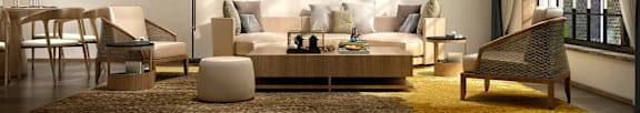 A modern living room with a white sofa, wooden chairs, and a yellow rug.