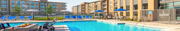 A swimming pool with sun loungers and apartment buildings in the background.