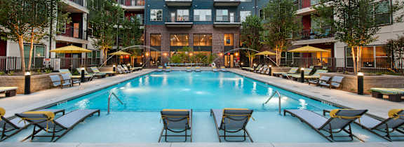 A swimming pool surrounded by lounge chairs and umbrellas in front of apartment buildings.