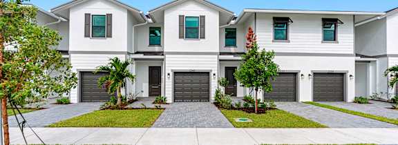 A large white house with a grey driveway and a red flower in the front yard.