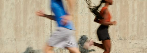 Two people running in front of a concrete wall.