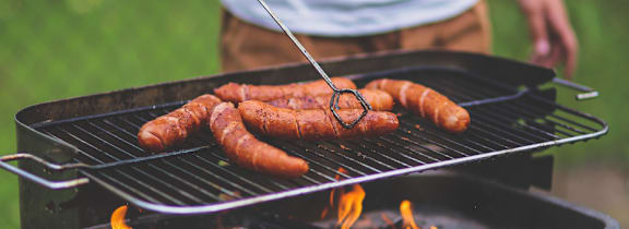 A person is grilling sausages on a barbecue.