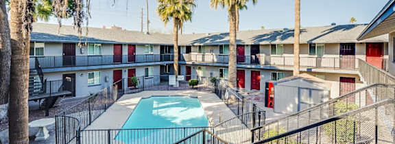 A pool surrounded by a black fence with palm trees in the background.