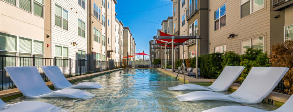 a swimming pool between two apartment buildings with white chairs at Mockingbird Flats, Dallas, 75206