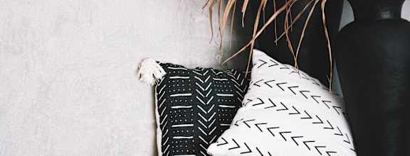 a black and white pillow on a shelf next to a black vase with a plant