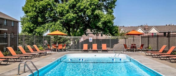 a swimming pool with orange chairs and a tree