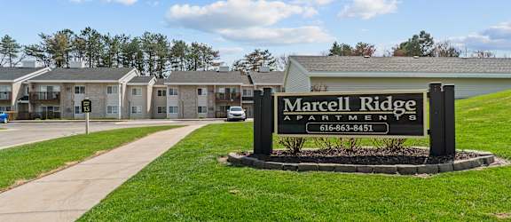 A sign for Marcel Ridge Apartments is in the foreground with apartment buildings in the background.