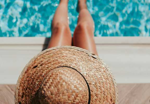A person wearing a straw hat is sitting by a pool.