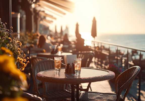 A table with a glass of water and a salt shaker on it is in the foreground of a sunny outdoor seating area.