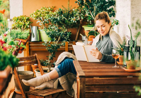 a woman sitting at a table reading a book on a patio
