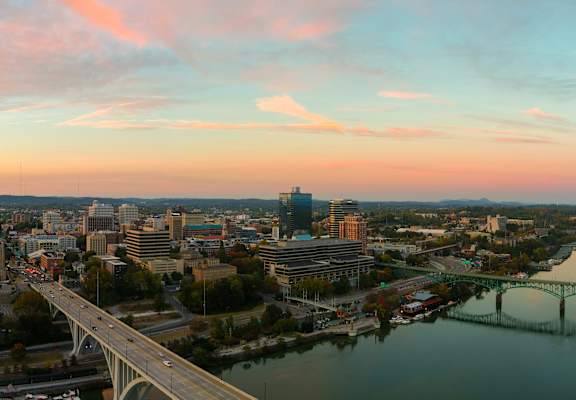 A cityscape with a river and a bridge during sunset.