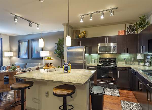 A kitchen island with bar stools, granite counters and stainless appliances