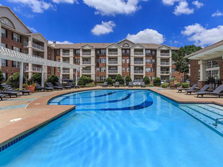 Outdoor swimming pool with lounge chairs and a multi-story apartment building at The Claremont
