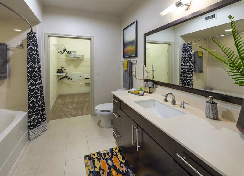A bathroom with a white sink, large mirror and tiled surround