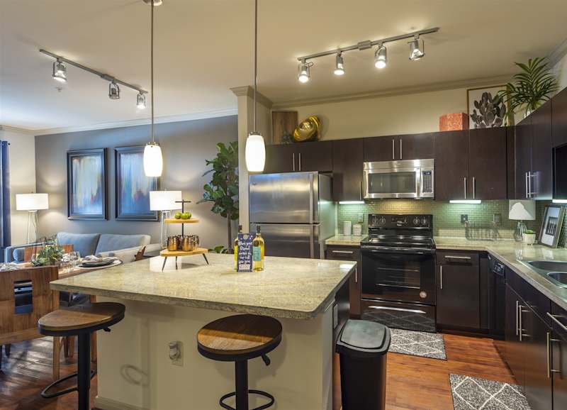 A kitchen island with bar stools, granite counters and stainless appliances