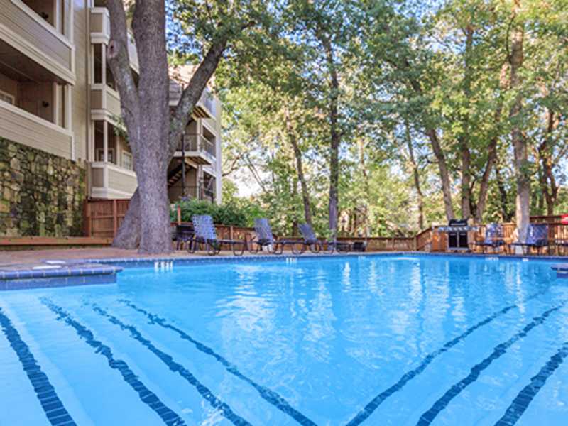 Tree-shaded swimming pool with lounge chairs and balcony apartments at Creekview Apartments