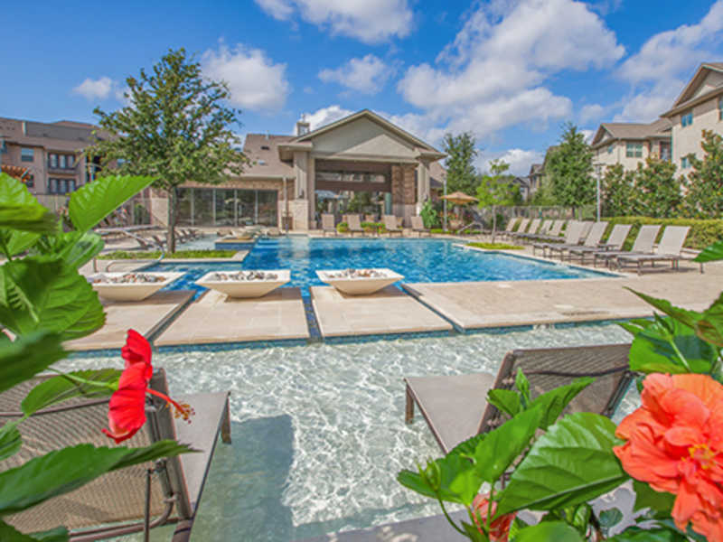 Resort-style pool with sun shelf, lounge chairs, and clubhouse pavilion at Ovation at Lewisville