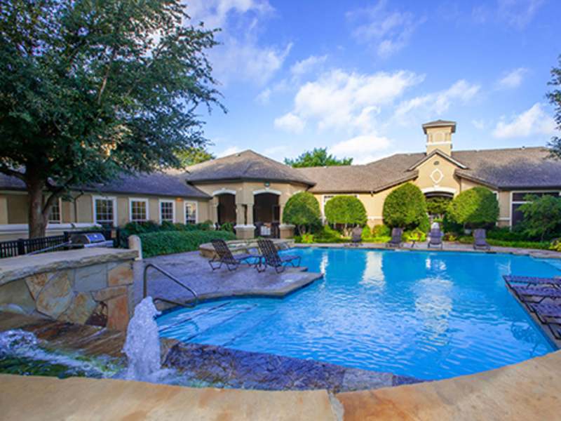 Pool with sun shelf, fountain feature, and clubhouse facade at Wade Crossing Apartment Homes