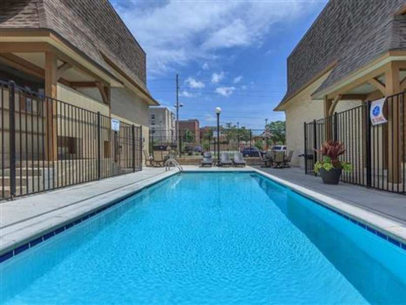 Rectangular turquoise community pool with lounge chairs, black metal fencing, and two-story beige apartment buildings