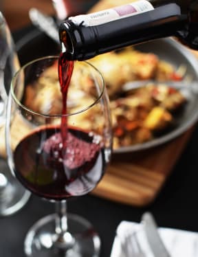 a glass of red wine with a plate of food in the background