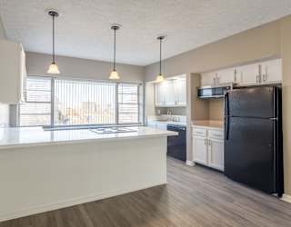 A kitchen with a black refrigerator and white cabinets at Lofts on Ormsby, Louisville, 40203
