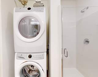 A white washing machine and dryer stacked on top of each other in a small laundry room.