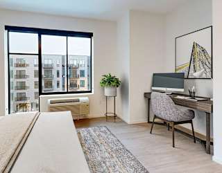 A bedroom with a large bed, a desk with a chair, and a window overlooking a cityscape.