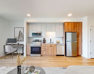 a living room with a kitchen with a refrigerator and a sink