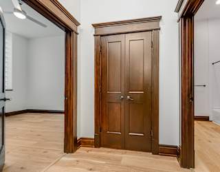 A wooden wardrobe stands in a room with a white wall and wooden floor.