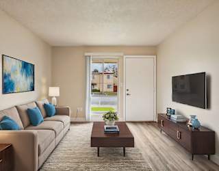 A living room with a brown couch, a coffee table, a painting, a lamp, a flat screen TV, and a door leading to a balcony.