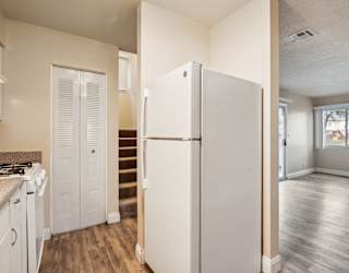 A white refrigerator in a kitchen with wood floors and a staircase.